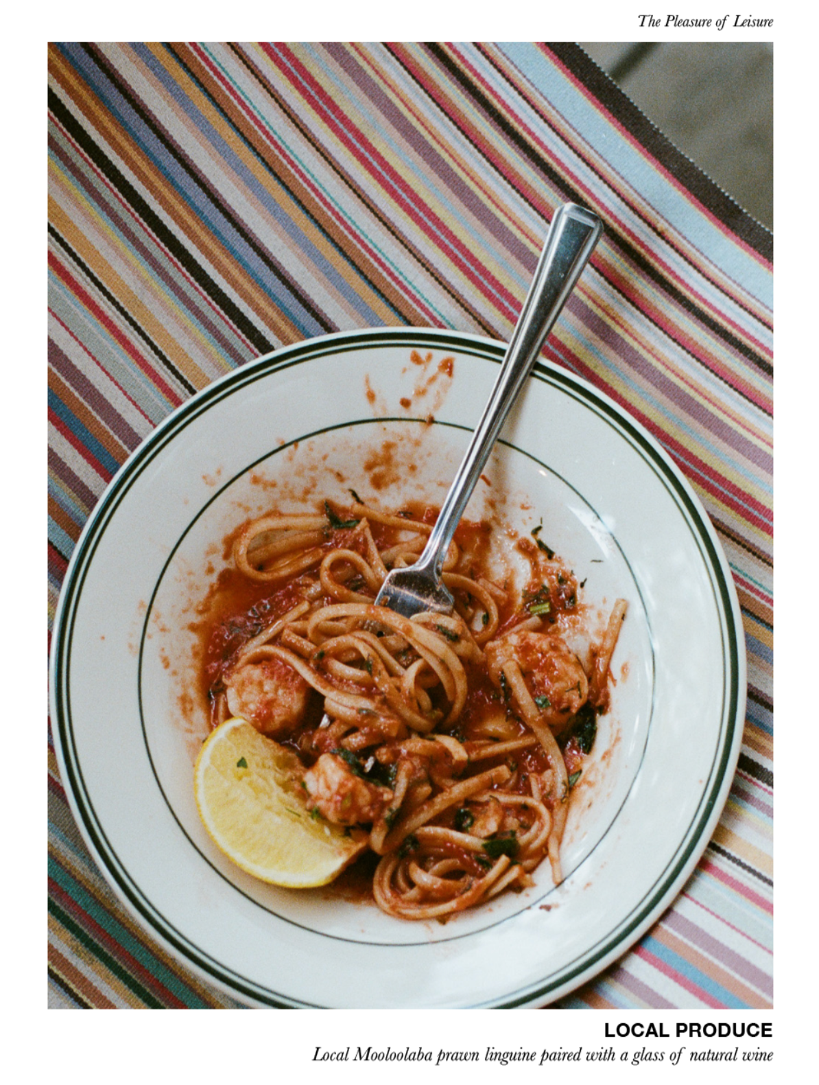 Plate of spaghetti with a fork and lemon wedge on a striped tablecloth, with text 'The Pleasure of Leisure' and 'LOCAL PRODUCE'.